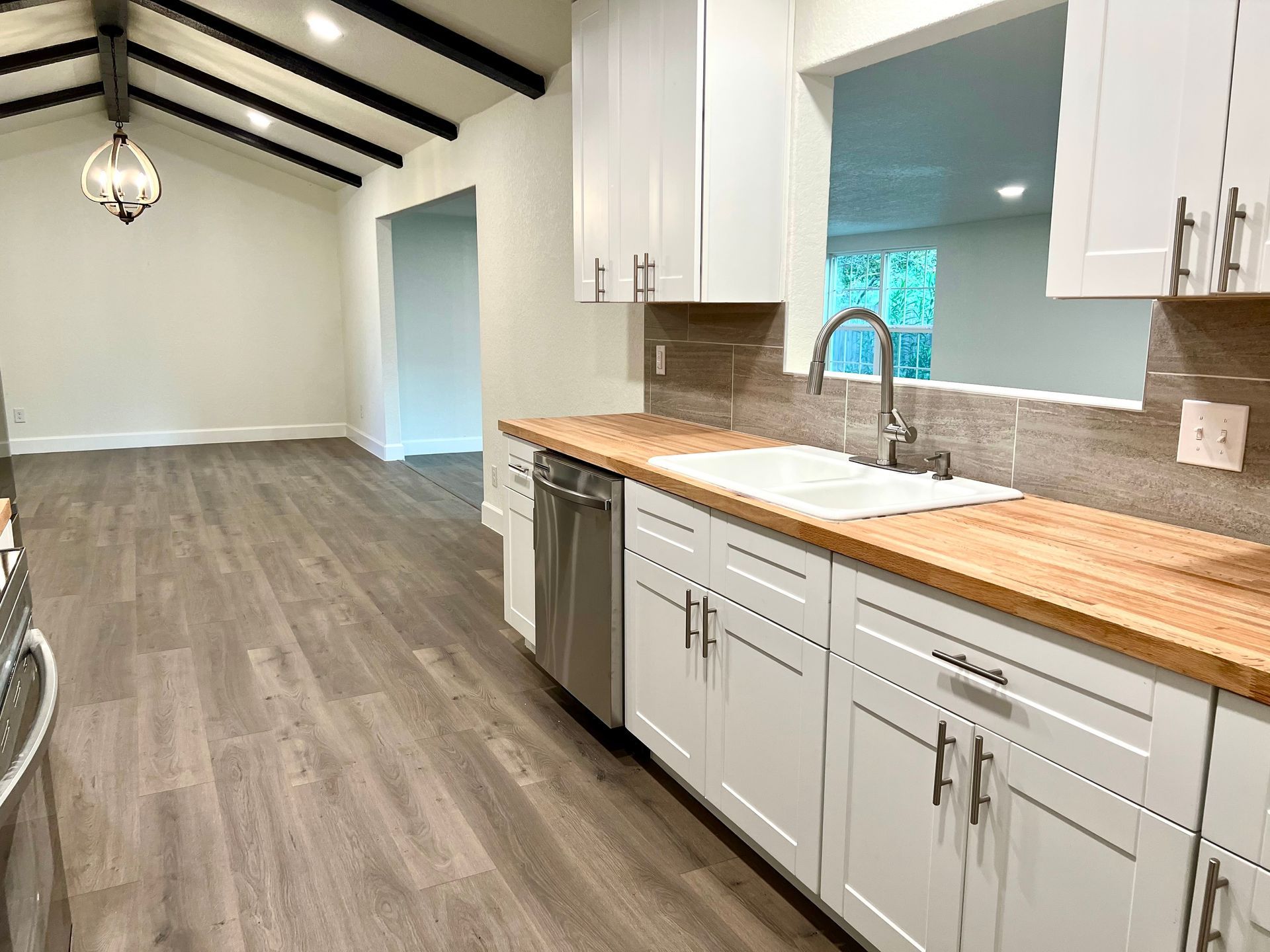 White kitchen with wooden countertop and stainless steel appliances, opening to living room.
