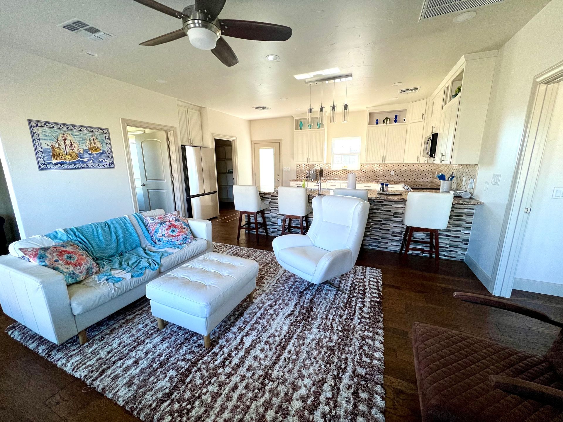 Living room with white furniture, wood floors, and a kitchen with a bar.
