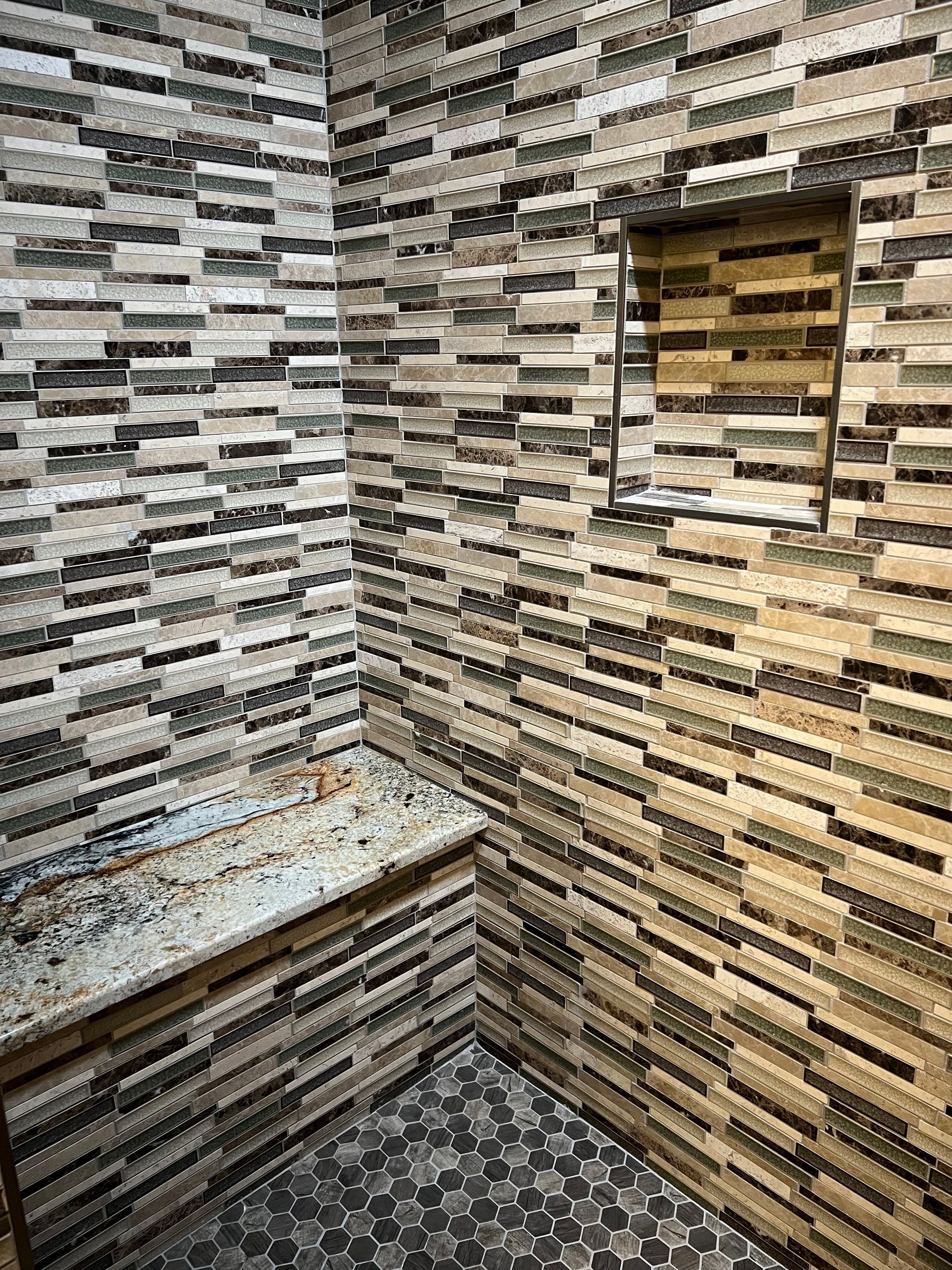 Shower interior with beige, brown, and gray tile. A built-in bench and recessed shelf.