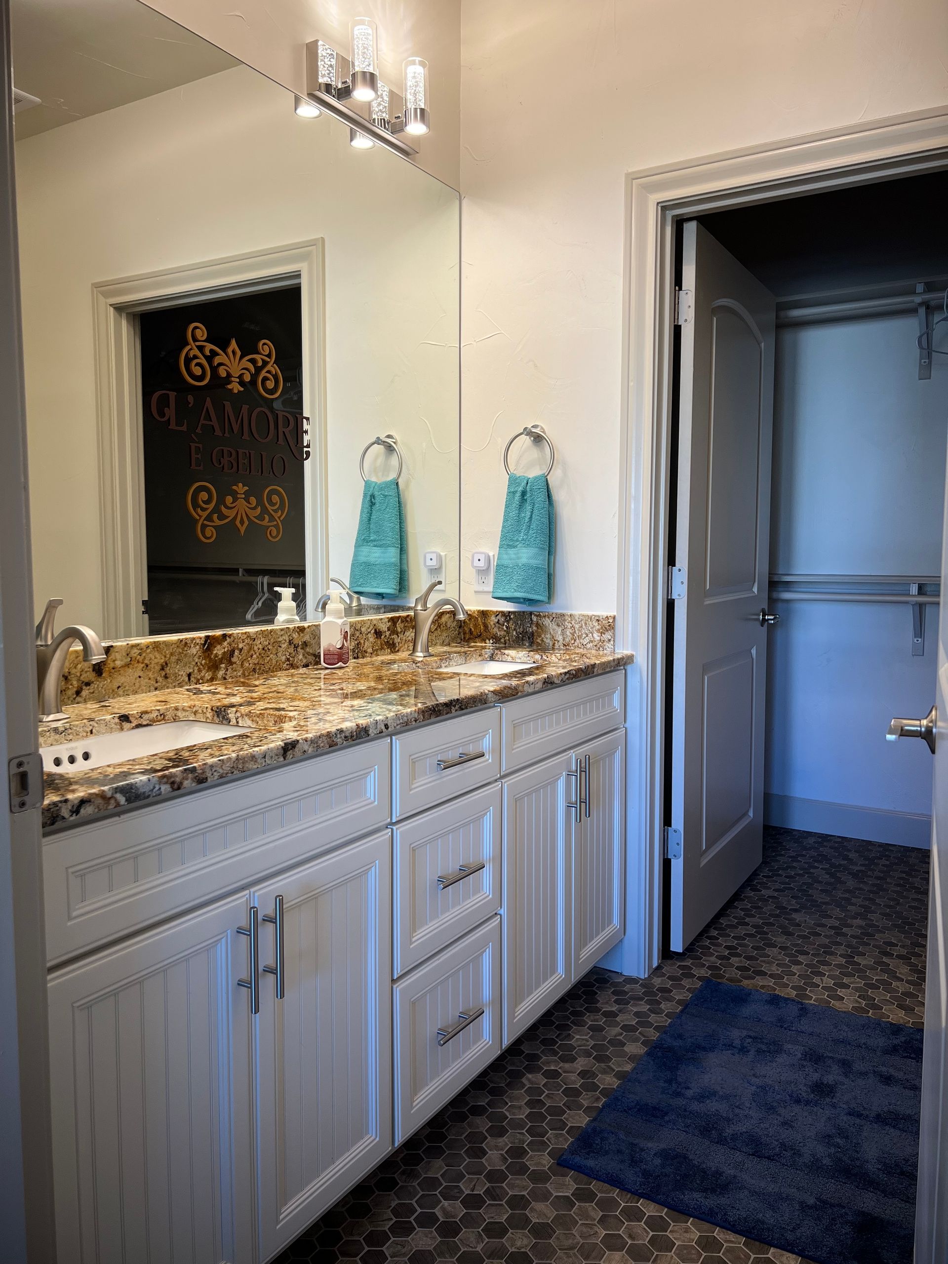 Bathroom with double vanity, granite countertop, blue towels, and closet.