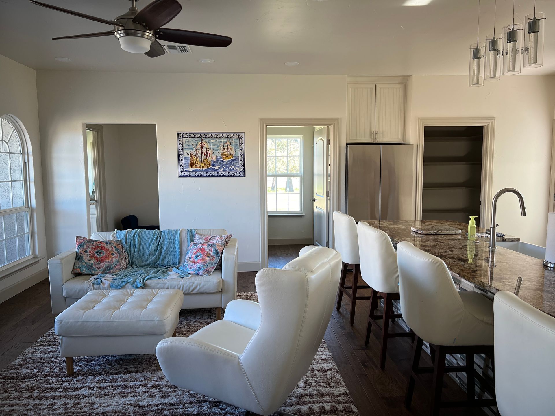 Living room with white furniture, kitchen island, and open doorways.