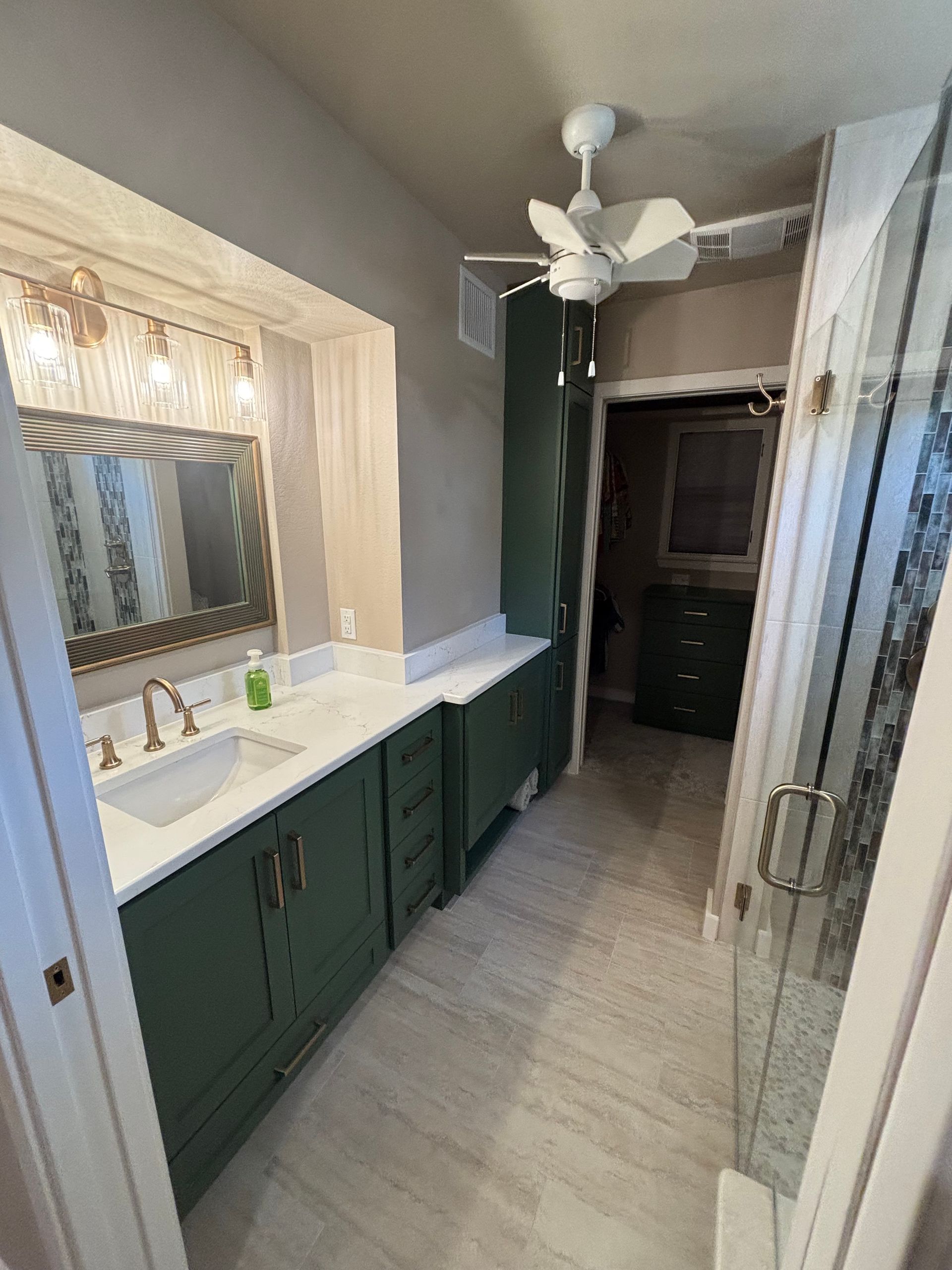Green bathroom cabinets and countertop with a sink. Tile floor and walk-in shower.