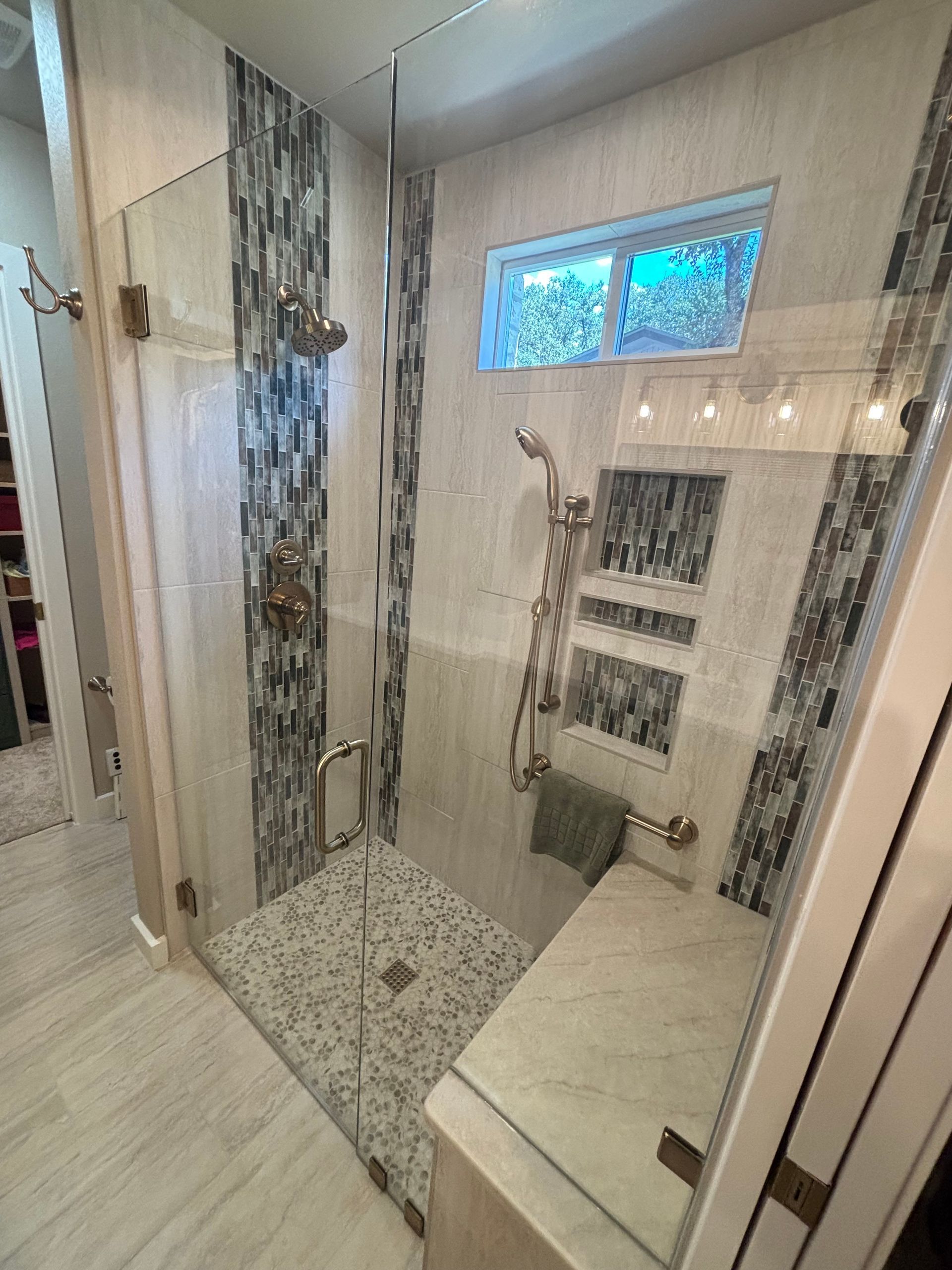 Spacious shower with glass door, bench, and various tile patterns in white, gray, and blue.