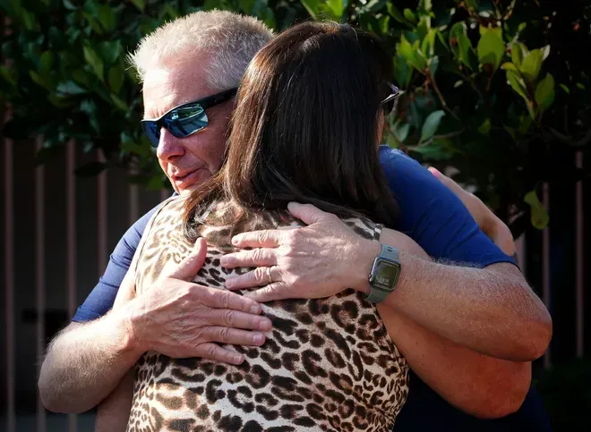 Man in sunglasses hugs woman with leopard print top outdoors.