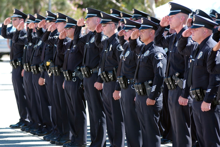 Police officers in dark uniforms saluting outdoors.