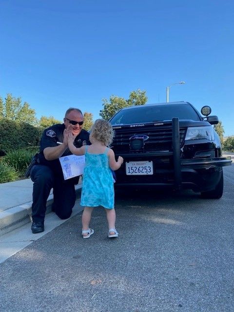 Police officer kneeling, giving a high five to a young child in front of a police car.