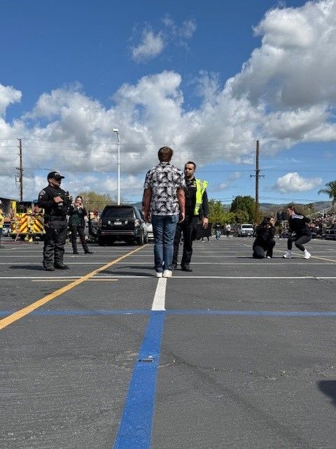 Man standing on a parking line while law enforcement observes. Other people are in the background, a car and a fire truck.