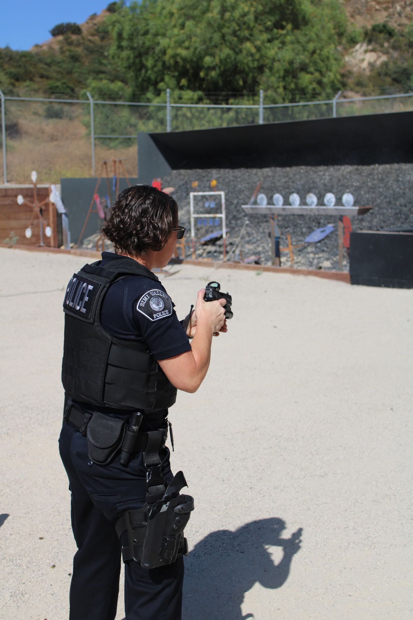 Police officer in uniform aims handgun at a shooting range target on a sunny day.