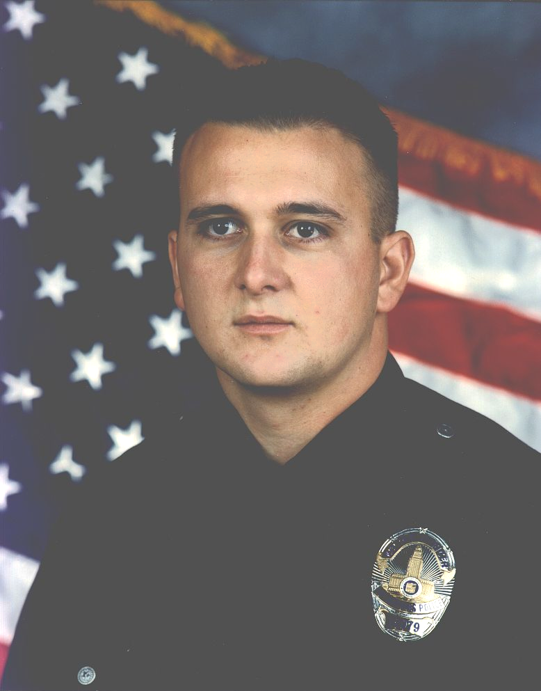 Police officer in uniform, posed against an American flag.