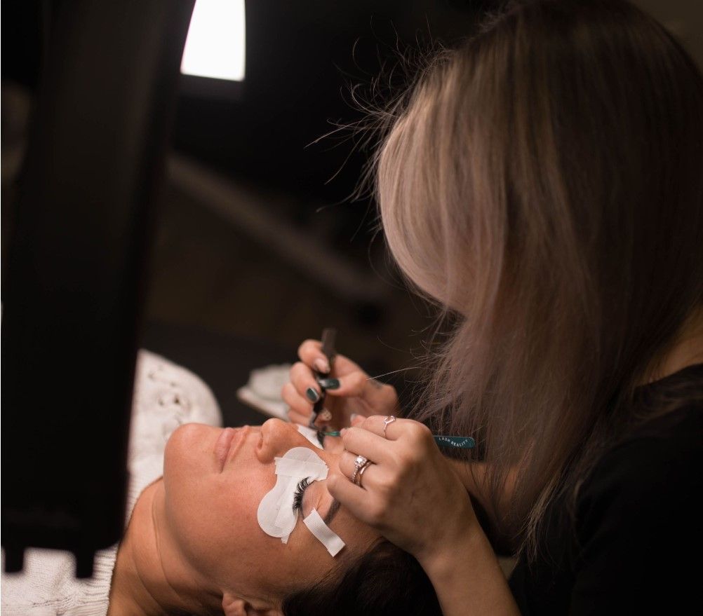 A woman with a towel wrapped around her head is smiling and touching her face.