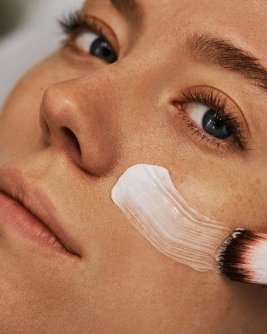 A woman is getting a cream applied to her face.