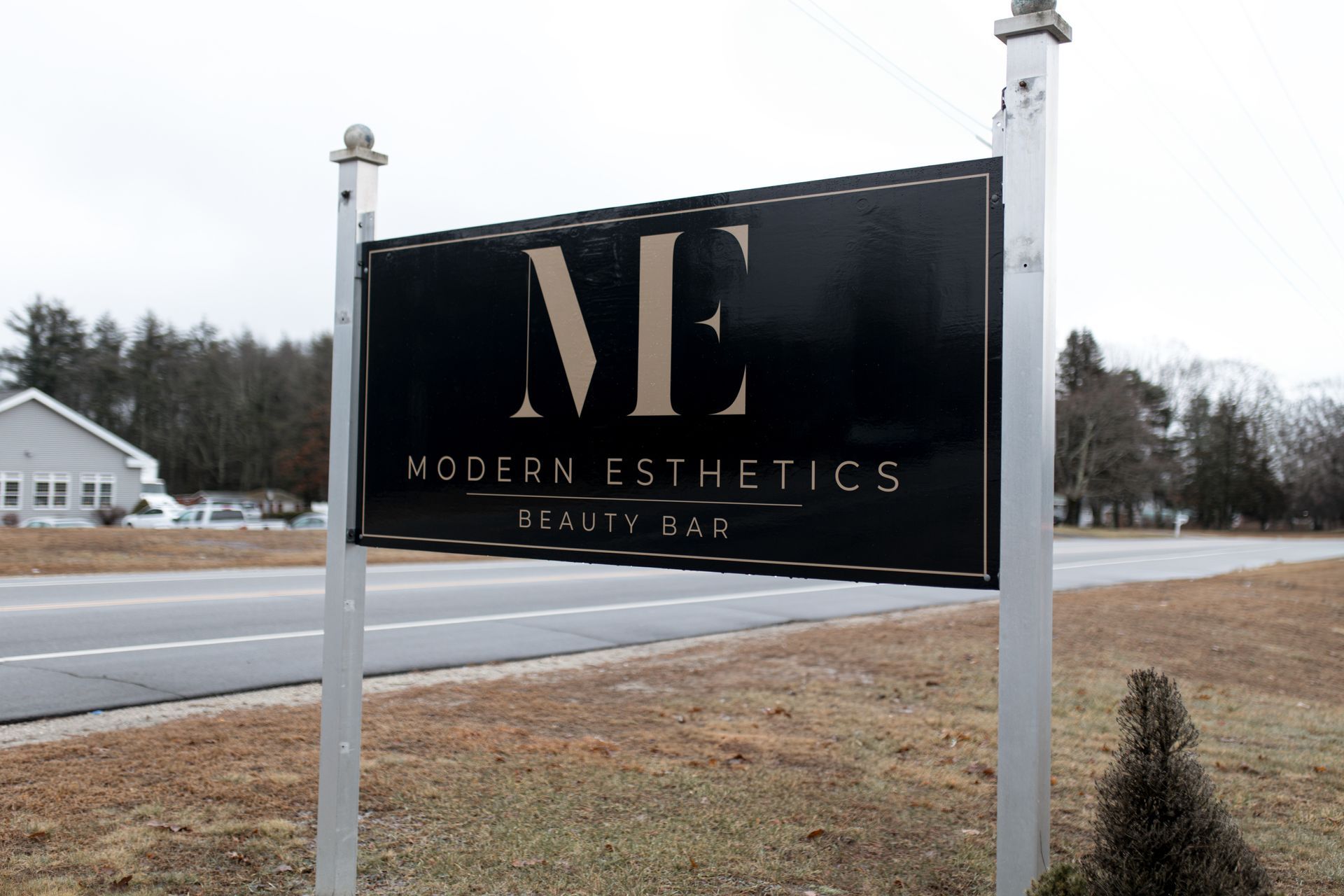 A sign for modern esthetics is hanging on a pole in front of a road.