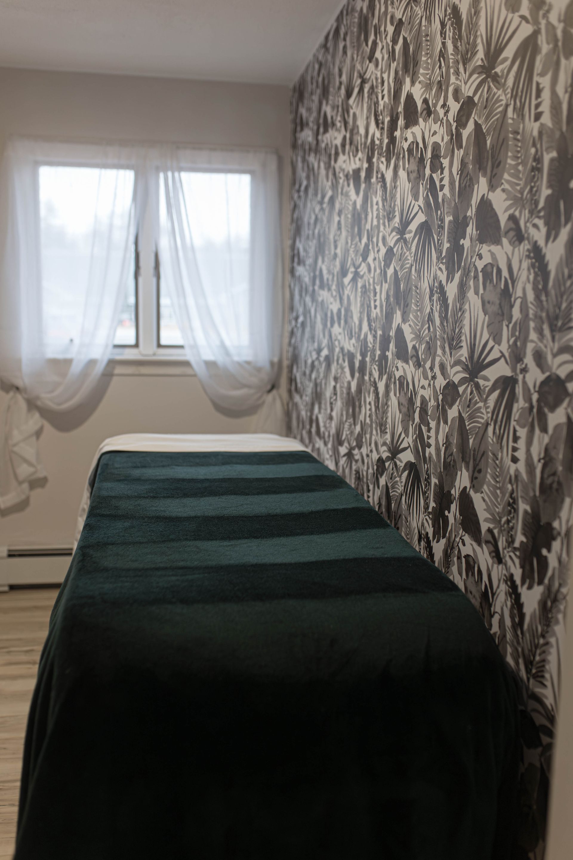 A bedroom with a bed and a window with a floral wallpaper on the wall.