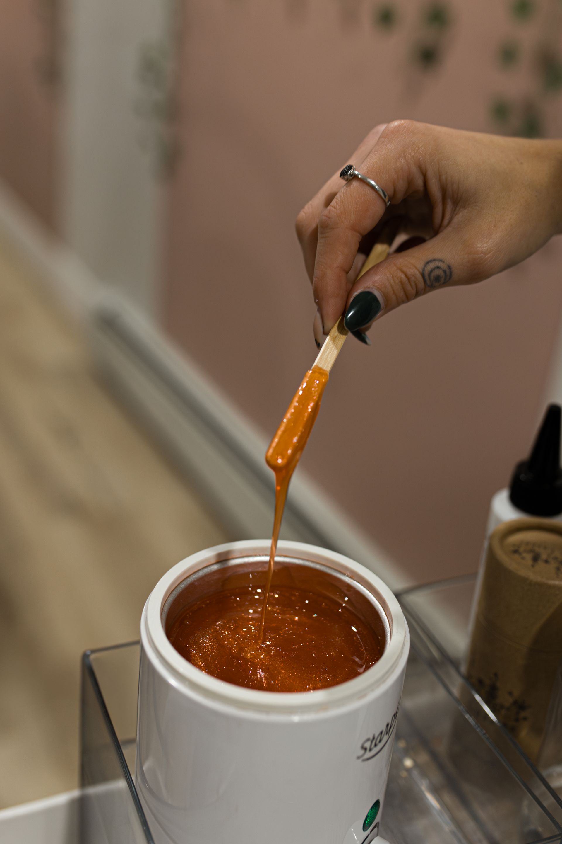 A person is pouring wax into a jar with a spatula.