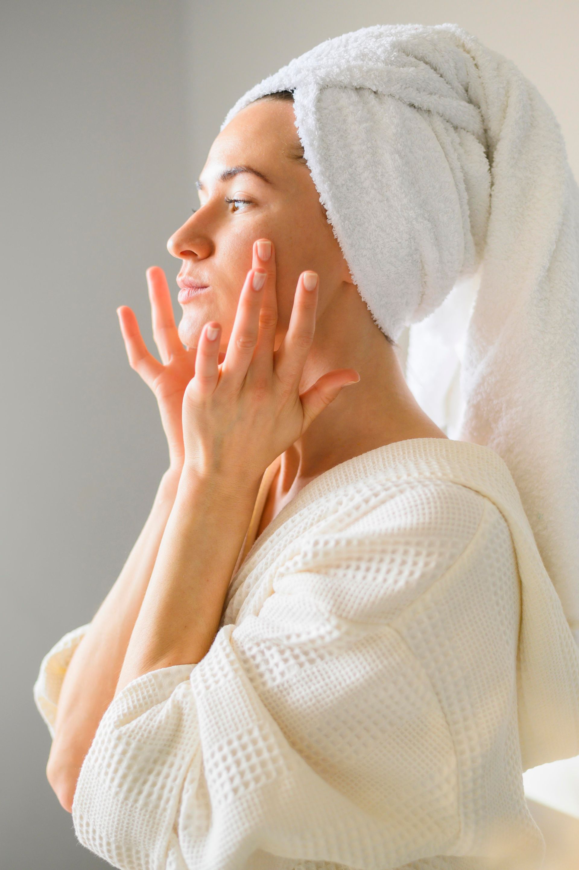 A woman with a towel wrapped around her head is looking at her face.