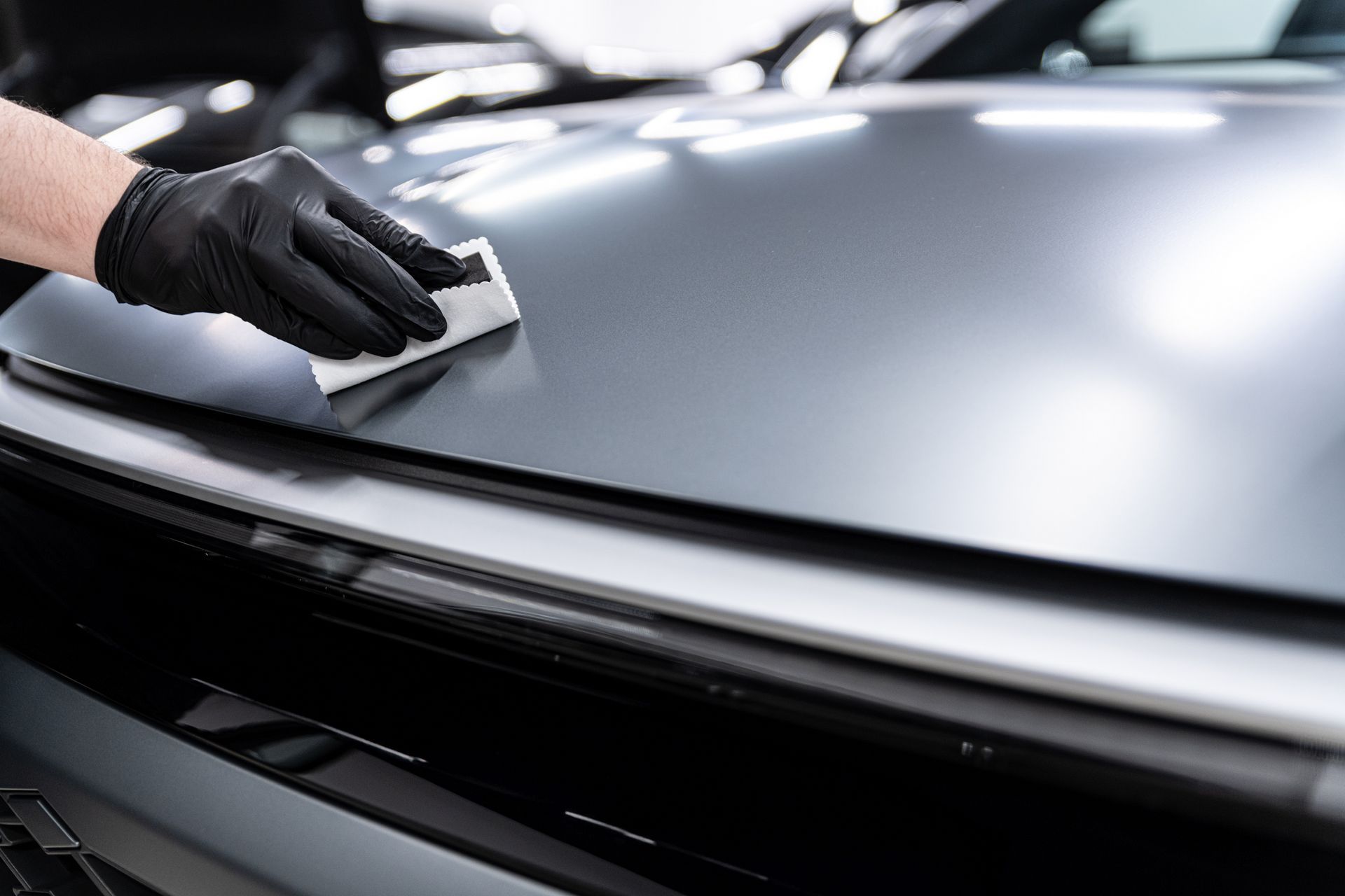 Gloved hand wiping a silver car hood with a cloth in a car wash or detailing setting