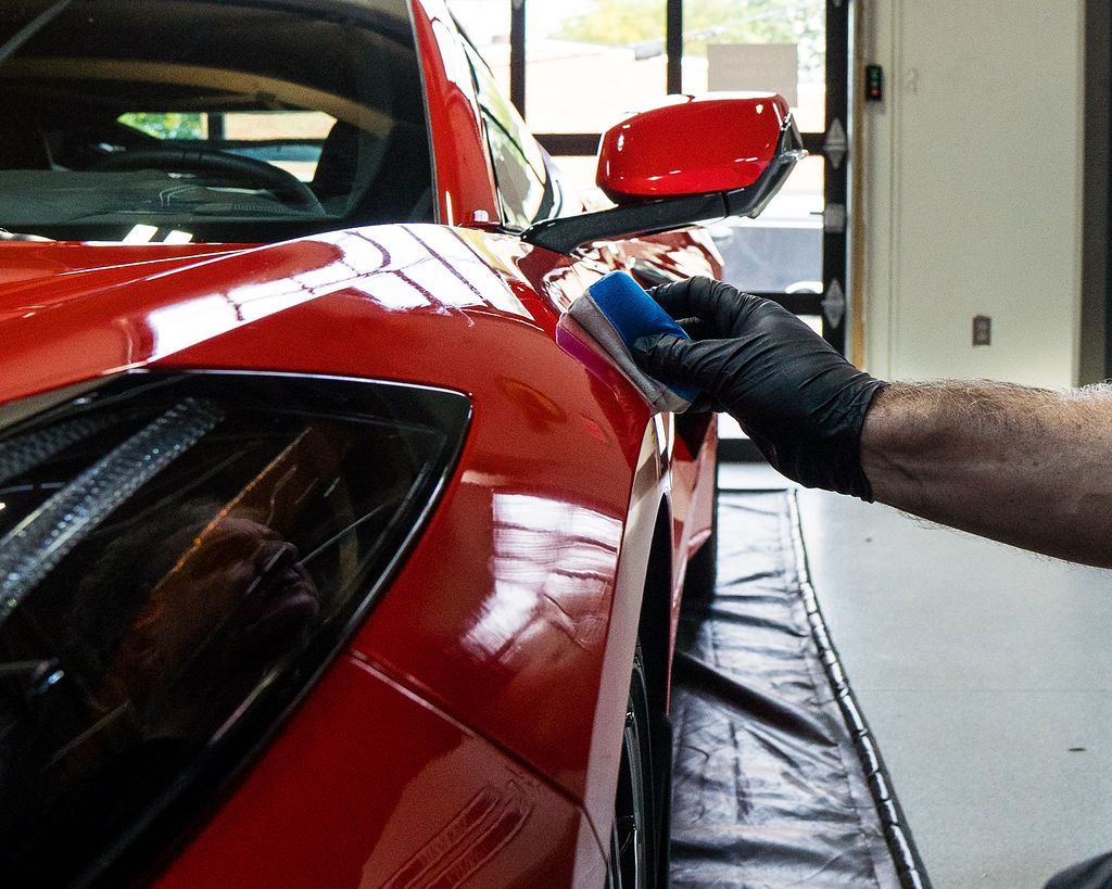 Gloved hand polishing a red sports car in a garage