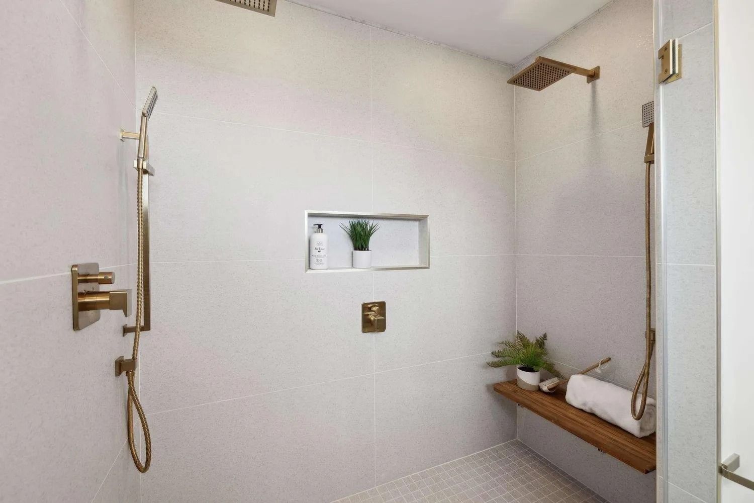 White tiled shower with gold fixtures, built-in shelf, bench, and glass door.