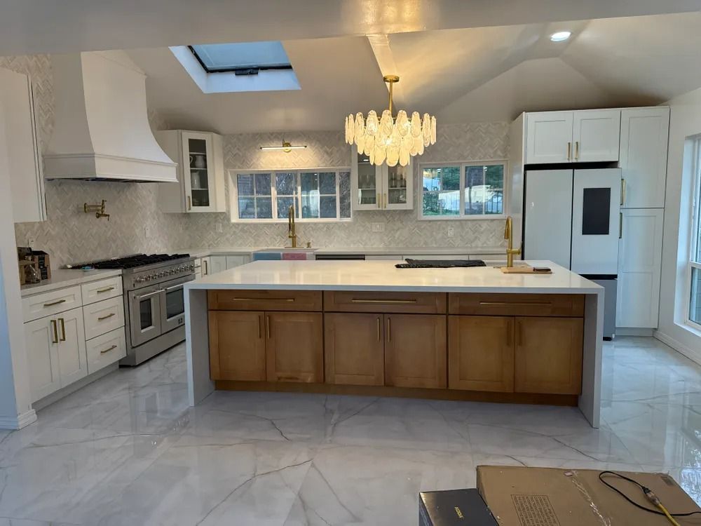 Kitchen with white cabinets, marble floors, large island, and a chandelier.