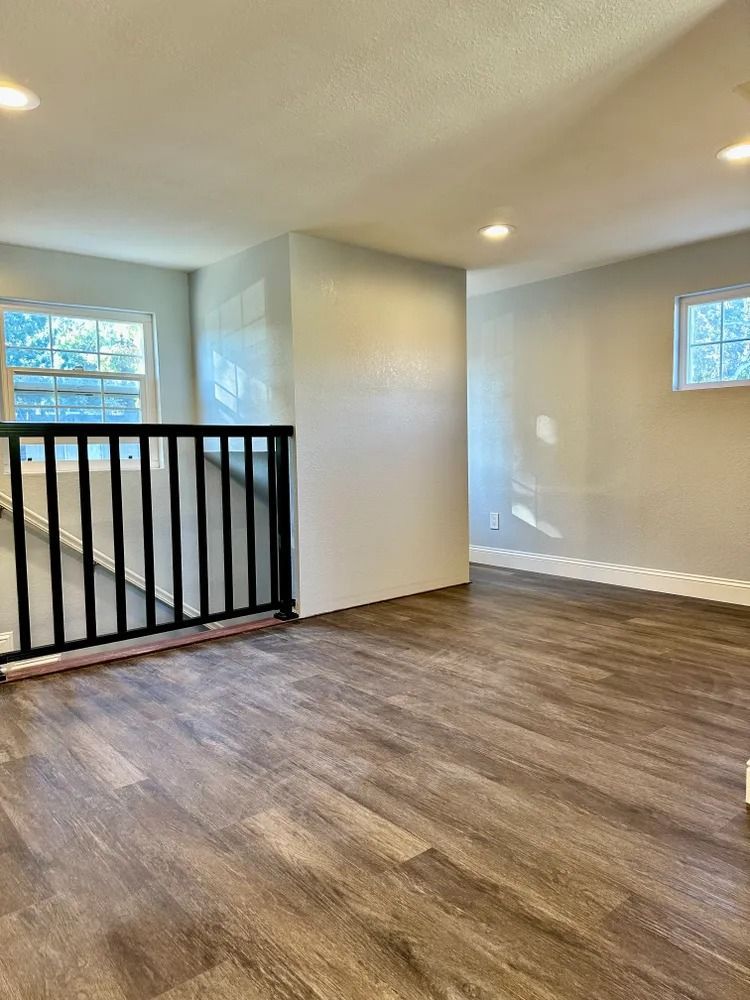 Interior view of a room with dark wood-look flooring, gray walls, a black railing, and two windows.