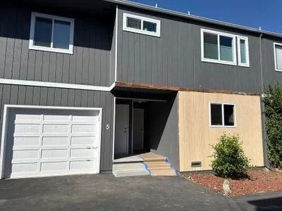 Gray townhome with white garage door and trim, tan accent wall, and front door.