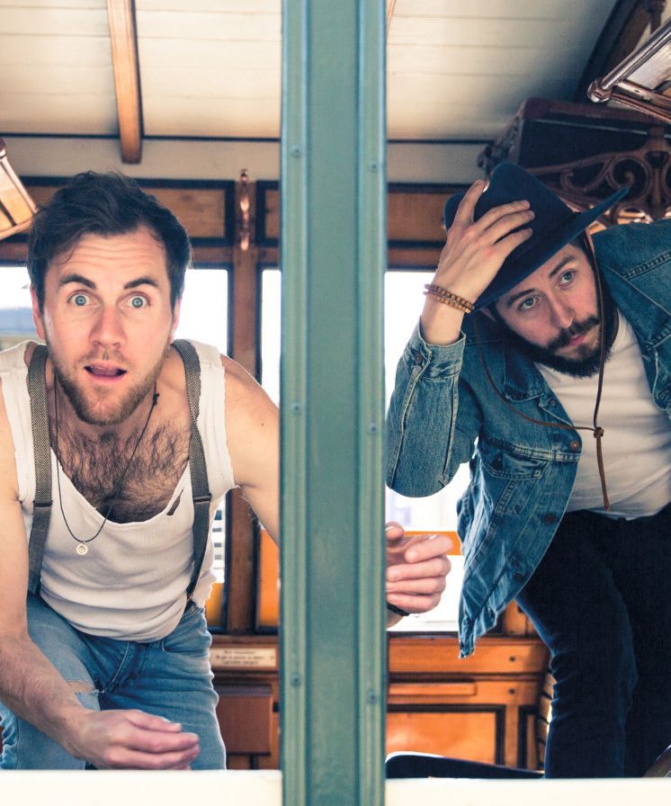 Folk-Duo: Oak Hill Road soft für stimmungsvolle Klänge.  Zwei Männer spähen durch eine senkrechte Stange. Einer im Tanktop sieht überrascht aus, der andere in Jeansjacke und Hut wirkt neugierig.