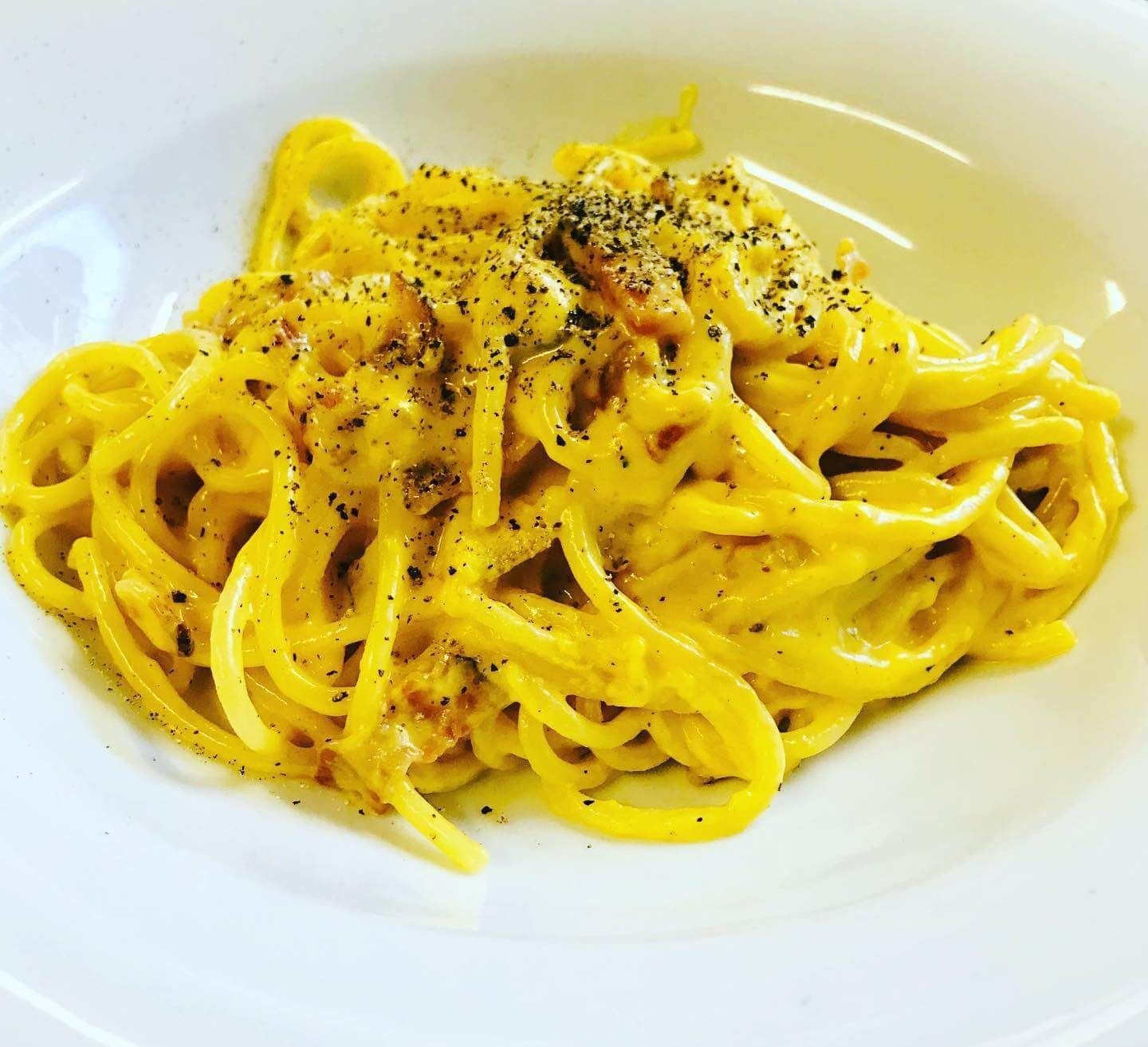 Un piatto bianco con sopra delle tagliatelle e una salsa gialla