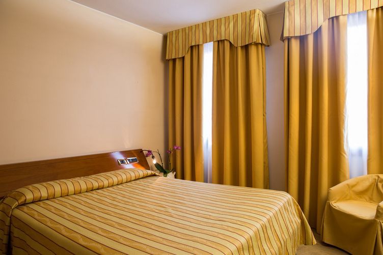 Una stanza d'albergo con un letto, una sedia e delle tende