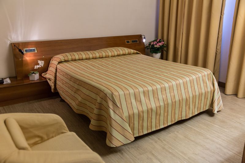 A hotel room with a bed , chair , nightstand and curtains.