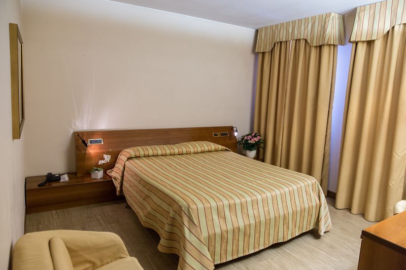 A hotel room with a bed , chair , nightstand and curtains.