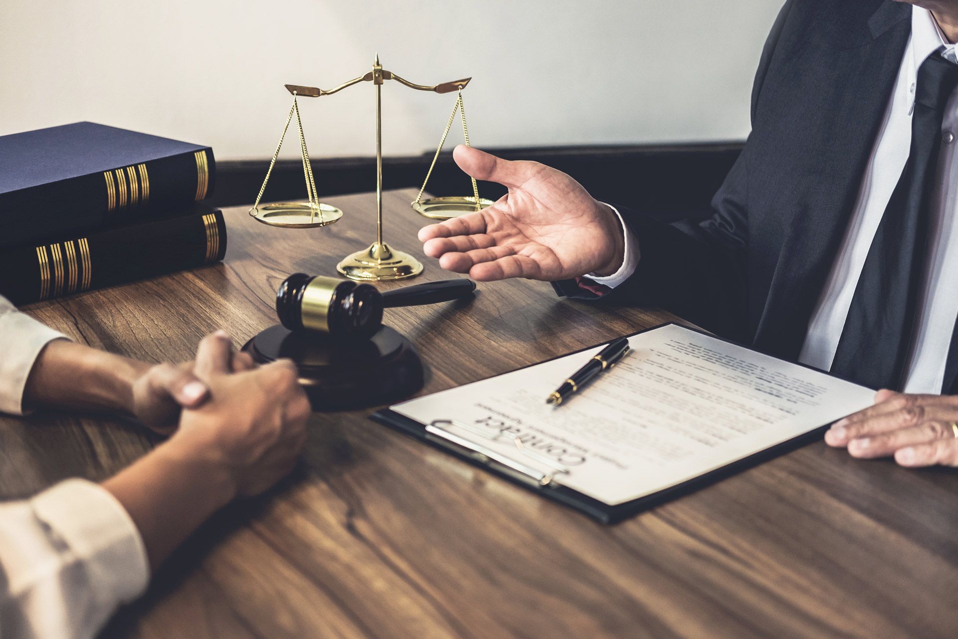 Lawyer gesturing to document; client listening at desk with gavel, scales, and books.