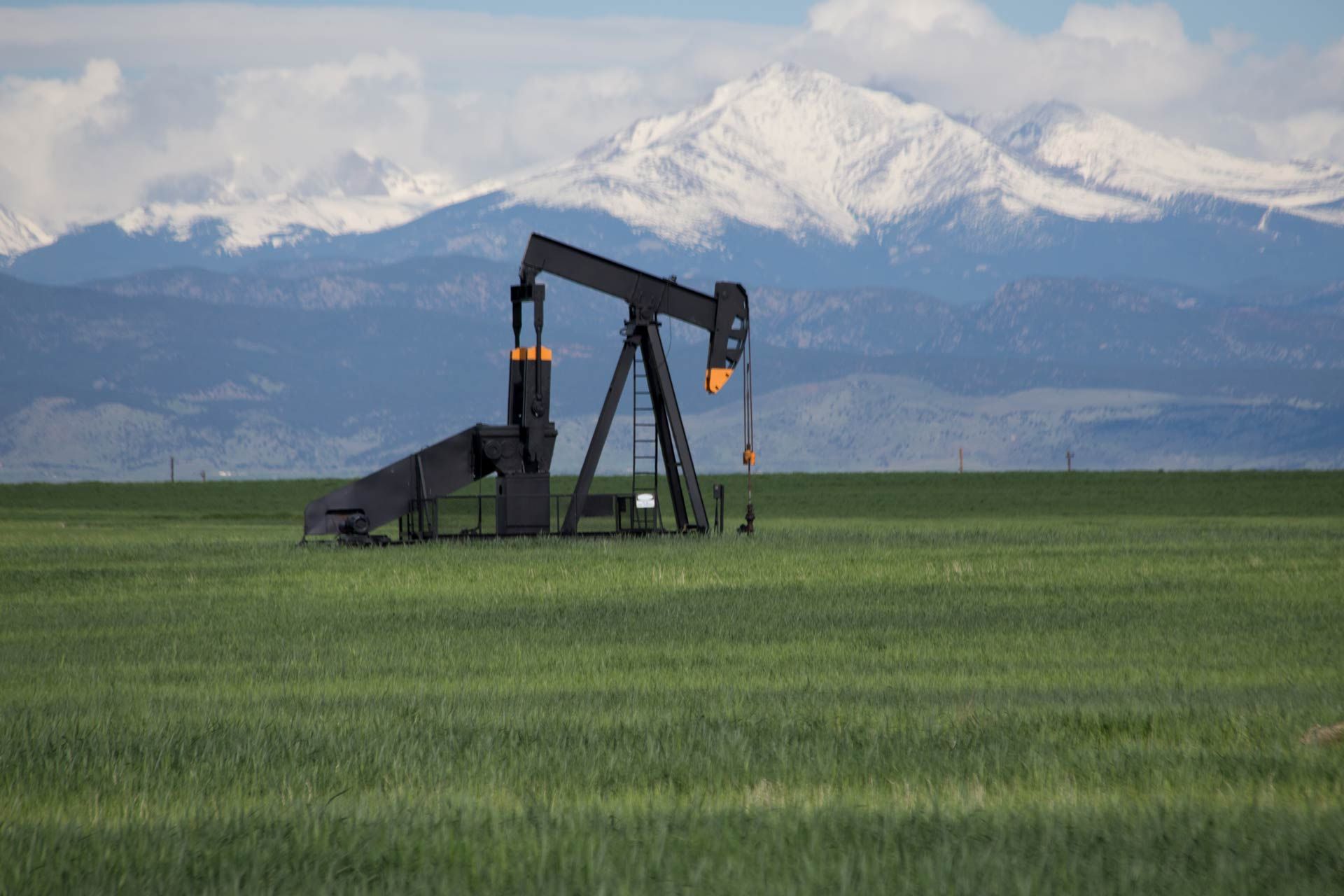 Oil pump jack in a green field with snow-capped mountains in the background.