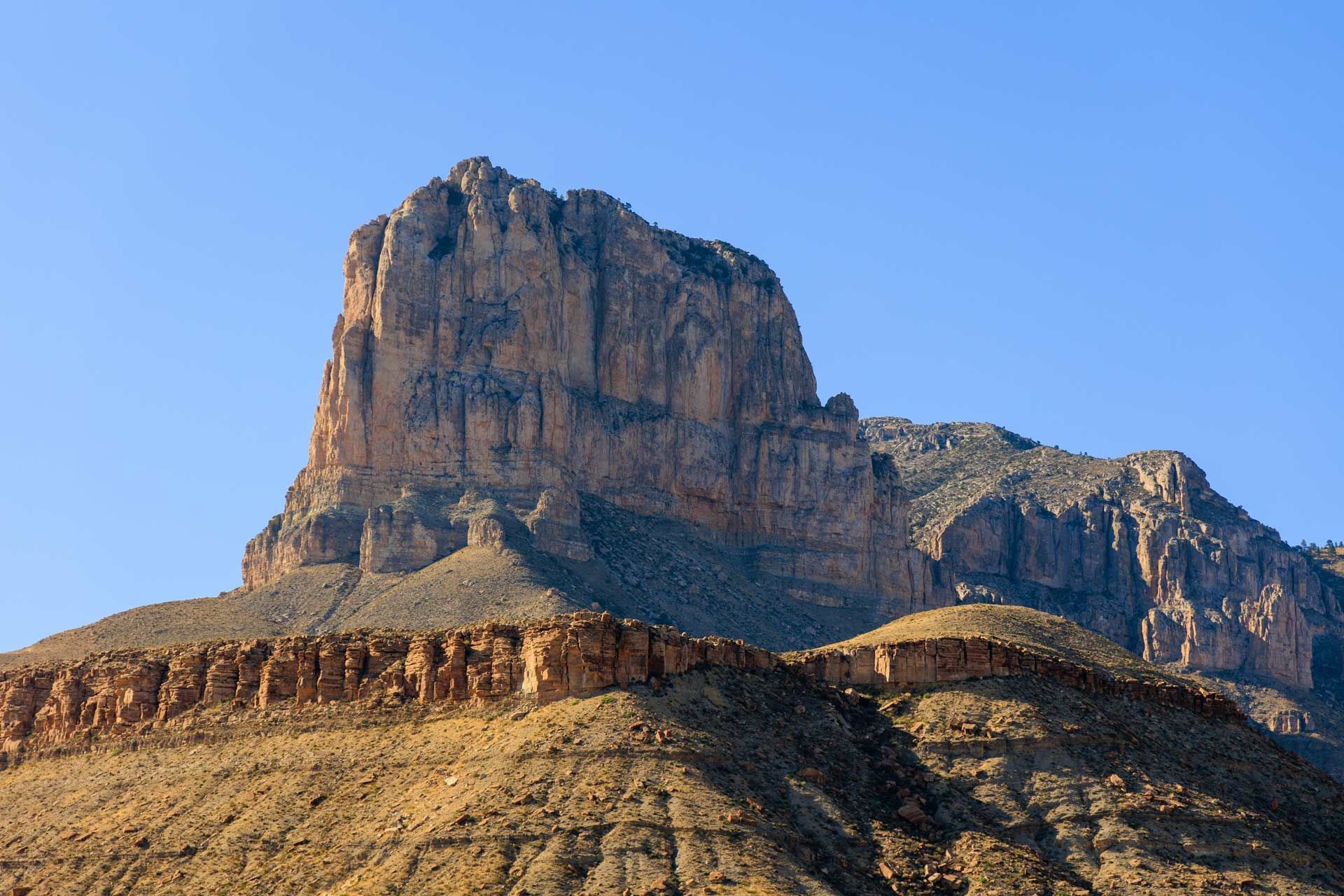 A large, flat-topped mountain with layered rock formations under a clear blue sky.