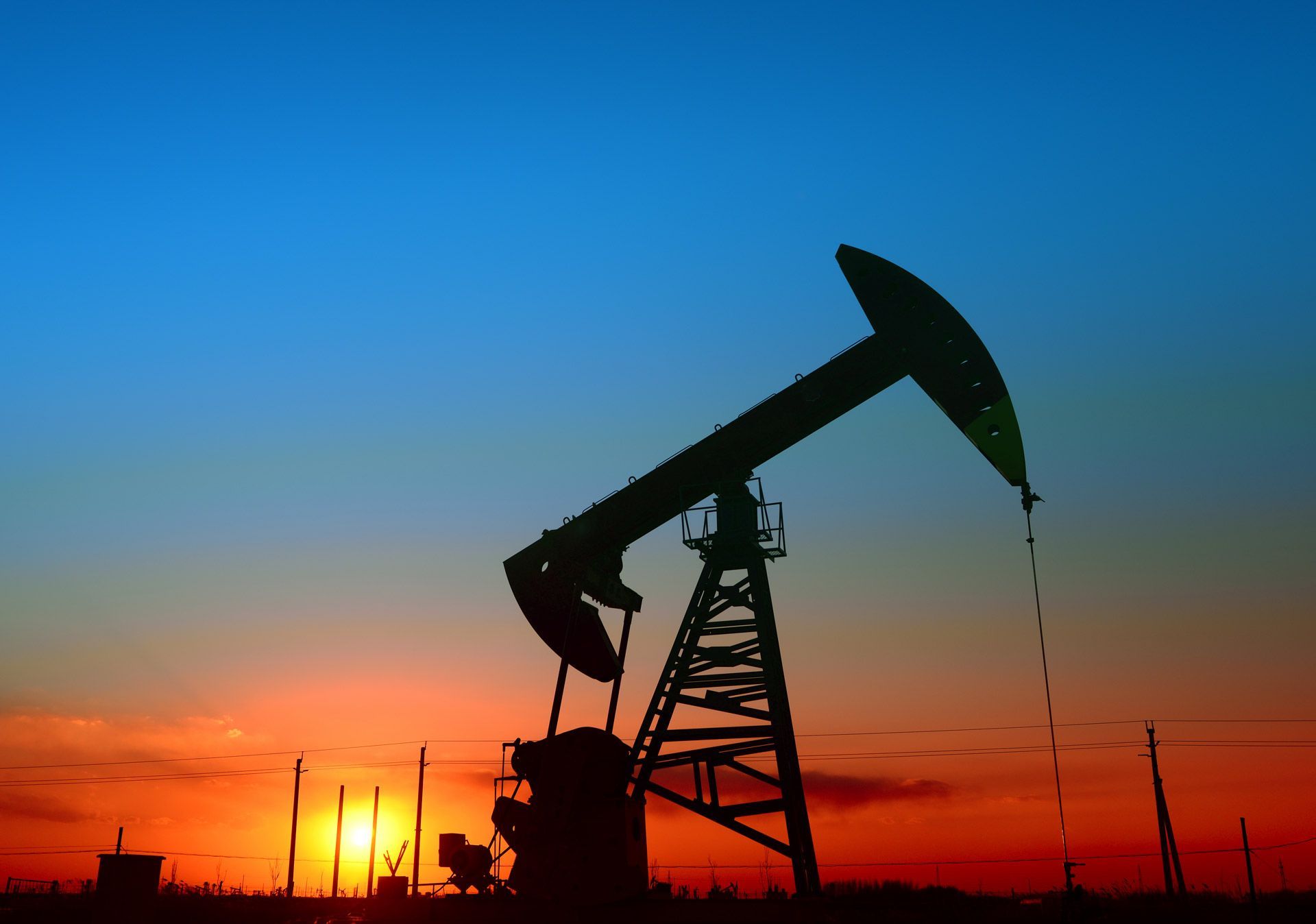 Oil pump jack silhouette against a colorful sunset sky.