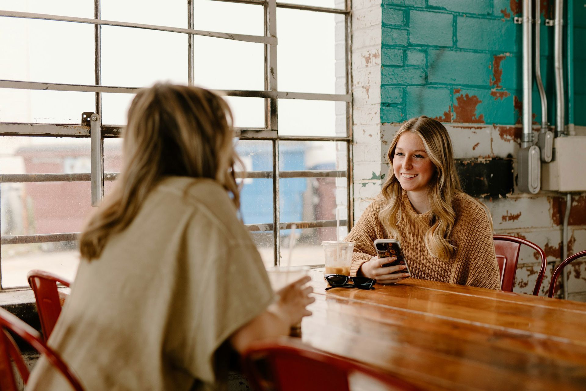 Two women are sitting at a table talking to each other and looking at their phones.