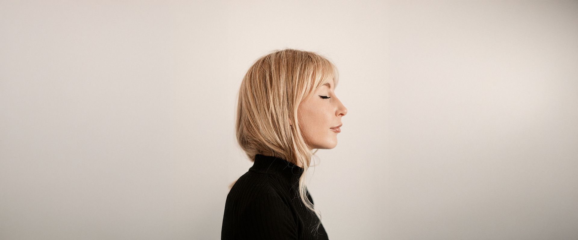 A woman with blonde hair is standing in front of a white wall.