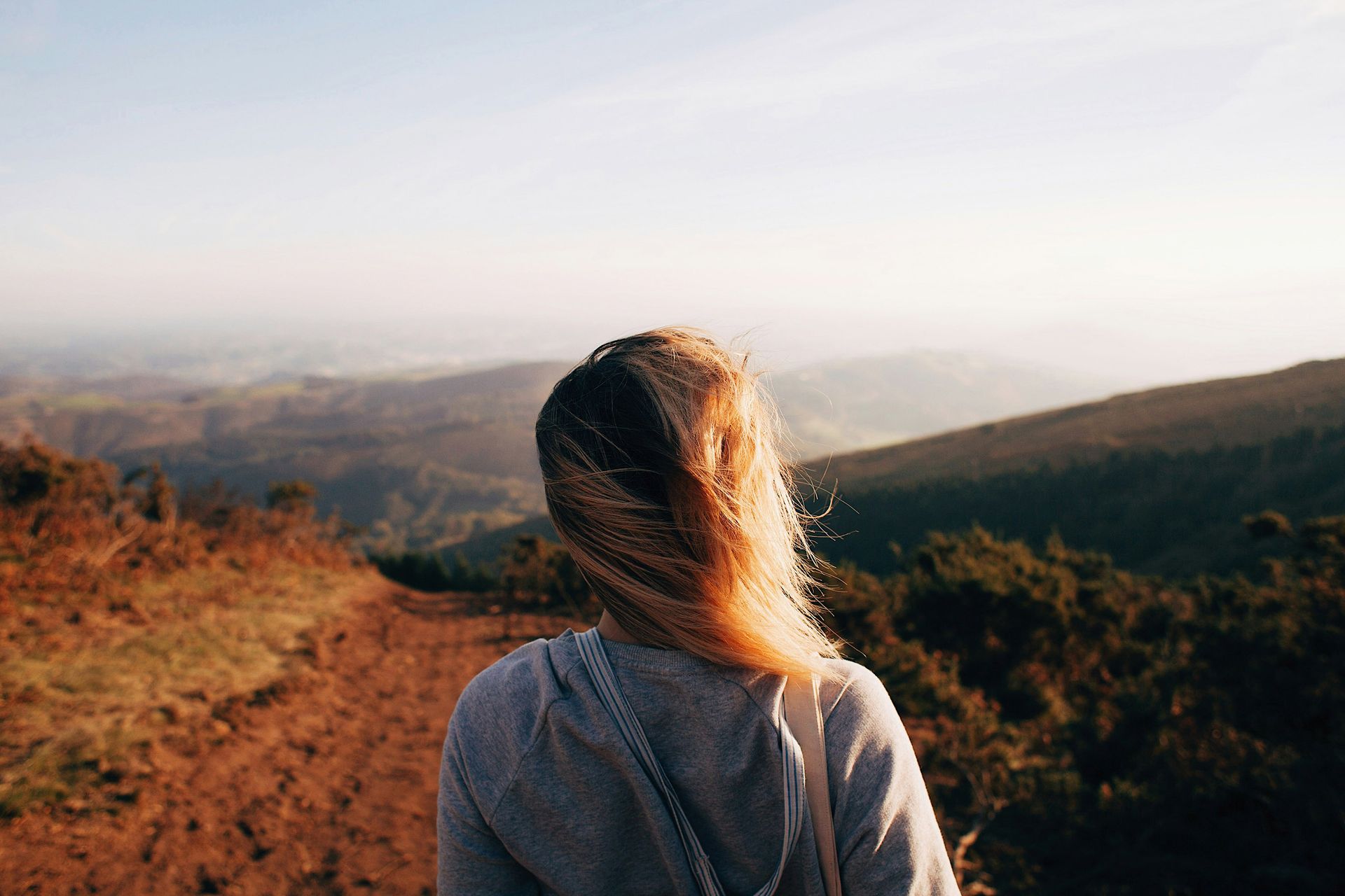 A woman is standing on top of a hill looking at the mountains.