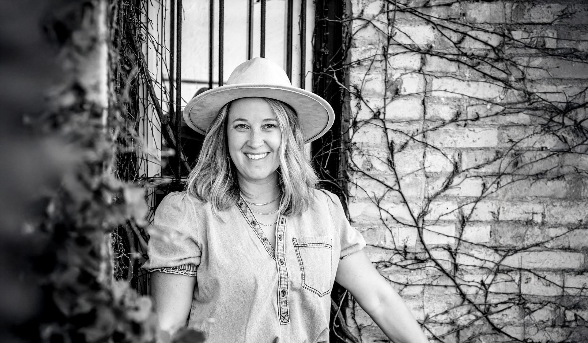 A black and white photo of a woman smiling in front of a palm tree.