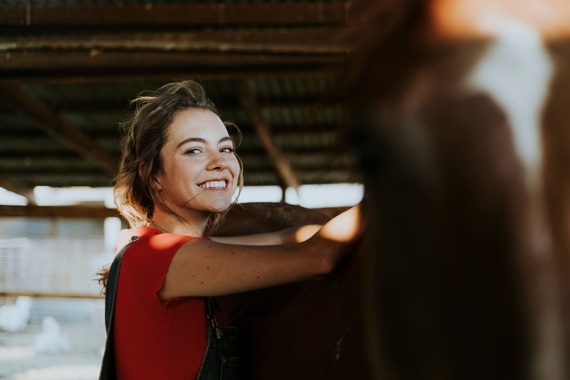 A woman is smiling while standing next to a horse in a barn.