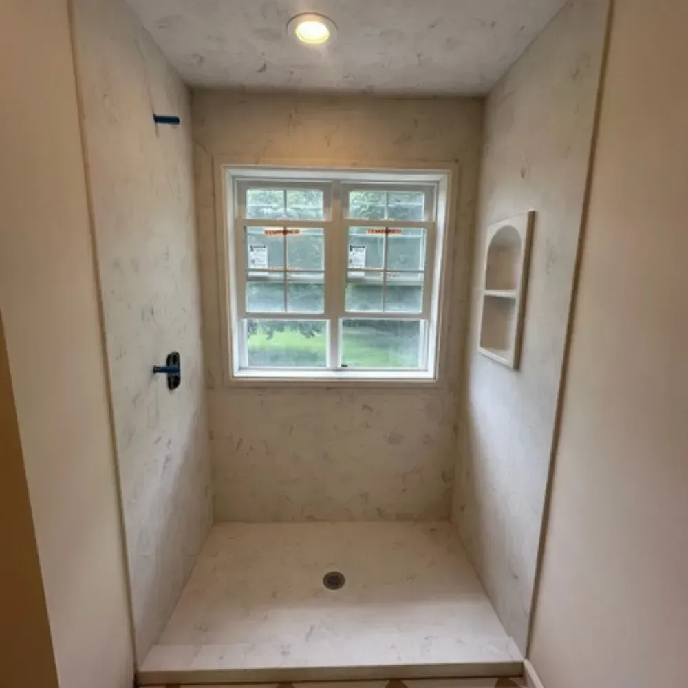 Shower stall with window, textured walls, built-in shelf, black faucet. Beige, off-white, and natural lighting by Syn-Mar