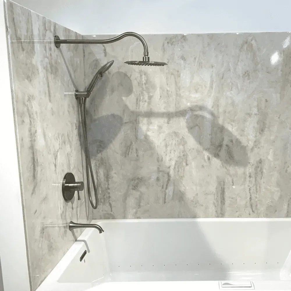 Shower fixture in a bathroom with a showerhead, handheld sprayer, and tub faucet against a marbled wall by Syn-Mar