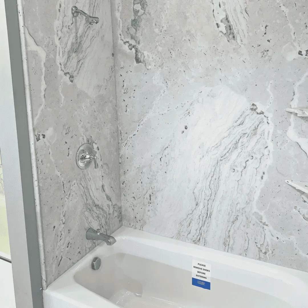 Bathtub with light gray marble-patterned shower walls and chrome fixtures by Syn-Mar