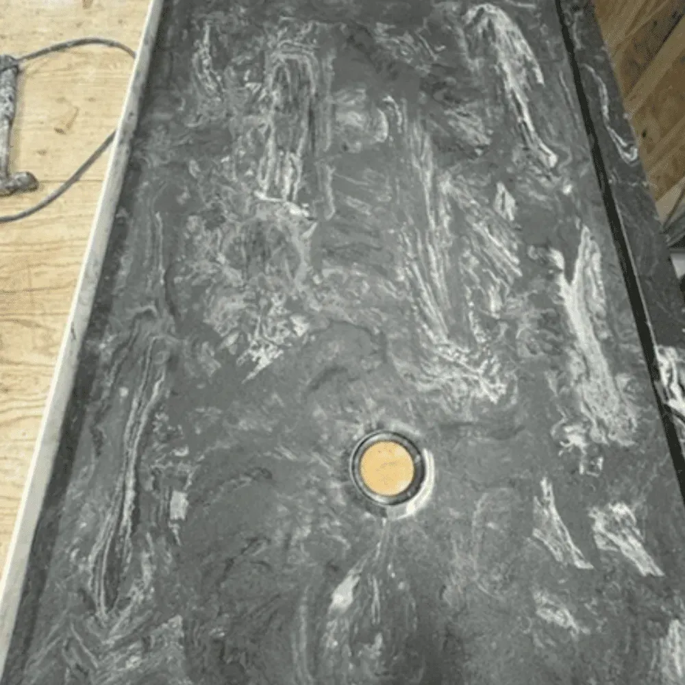 Dark gray shower base with white veining and a central drain by Syn-Mar