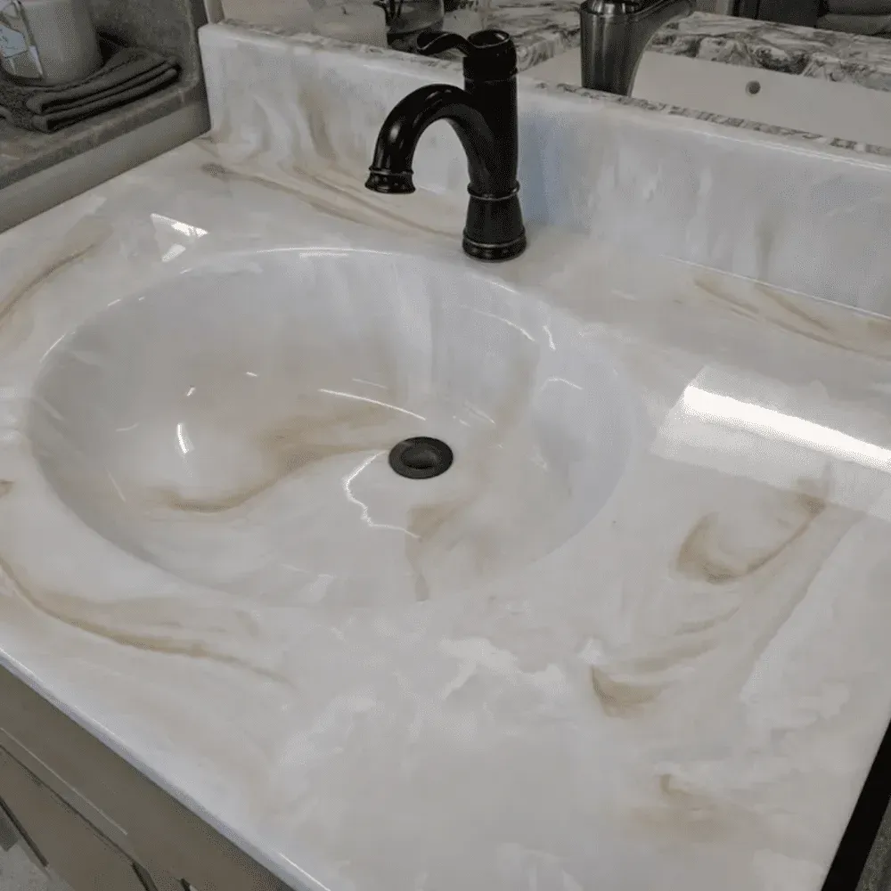 White bathroom sink with brown swirl pattern countertop and dark faucet by Syn-Mar