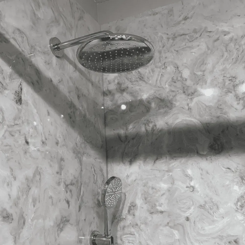 Showerhead in a marble-tiled shower, with a smaller handheld showerhead by Syn-Mar