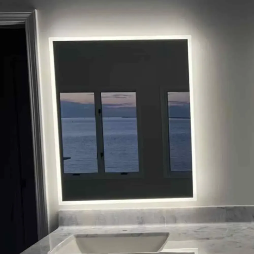 Lit mirror above a bathroom sink reflecting a view of windows and the ocean by Syn-Mar