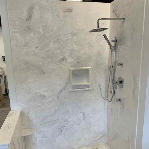 Shower with white marble-like walls, chrome fixtures, built-in soap dish, and a bench by Syn-Mar