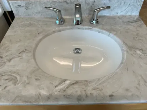 Bathroom sink with oval basin, chrome fixtures, and marbled countertop by Syn-Mar