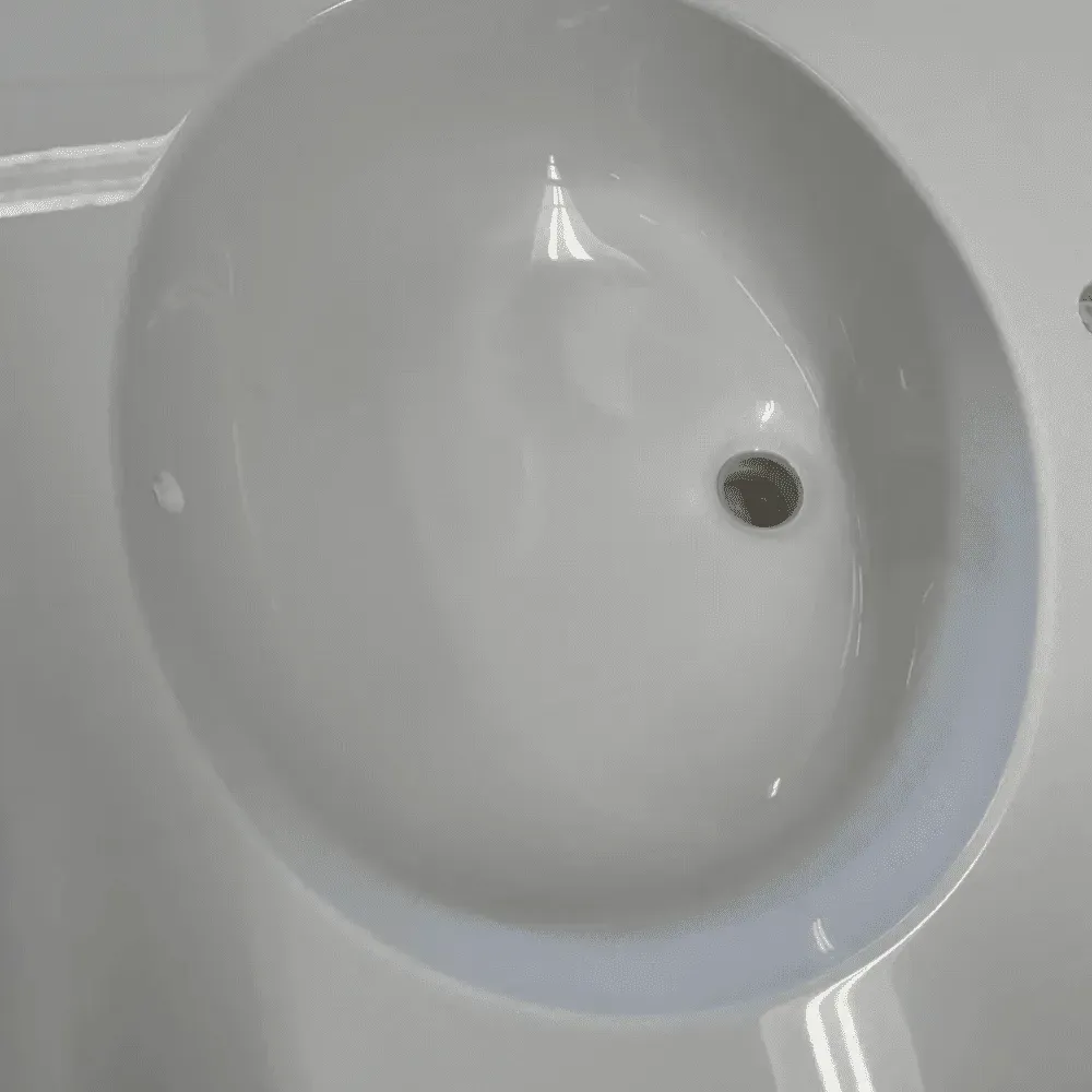 White, oval-shaped bathroom sink with drain. Water droplets and subtle reflections are visible by Syn-Mar