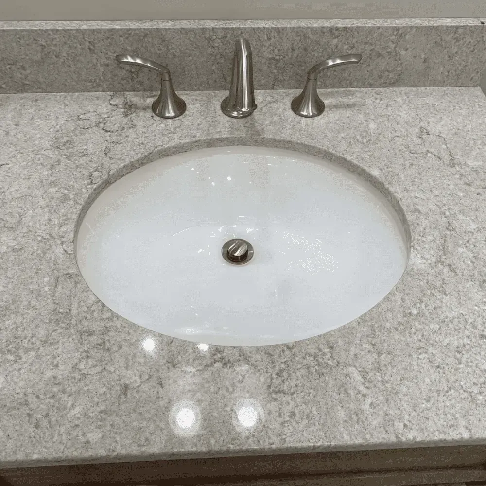 Oval white sink and faucet on a speckled gray countertop by Syn-Mar